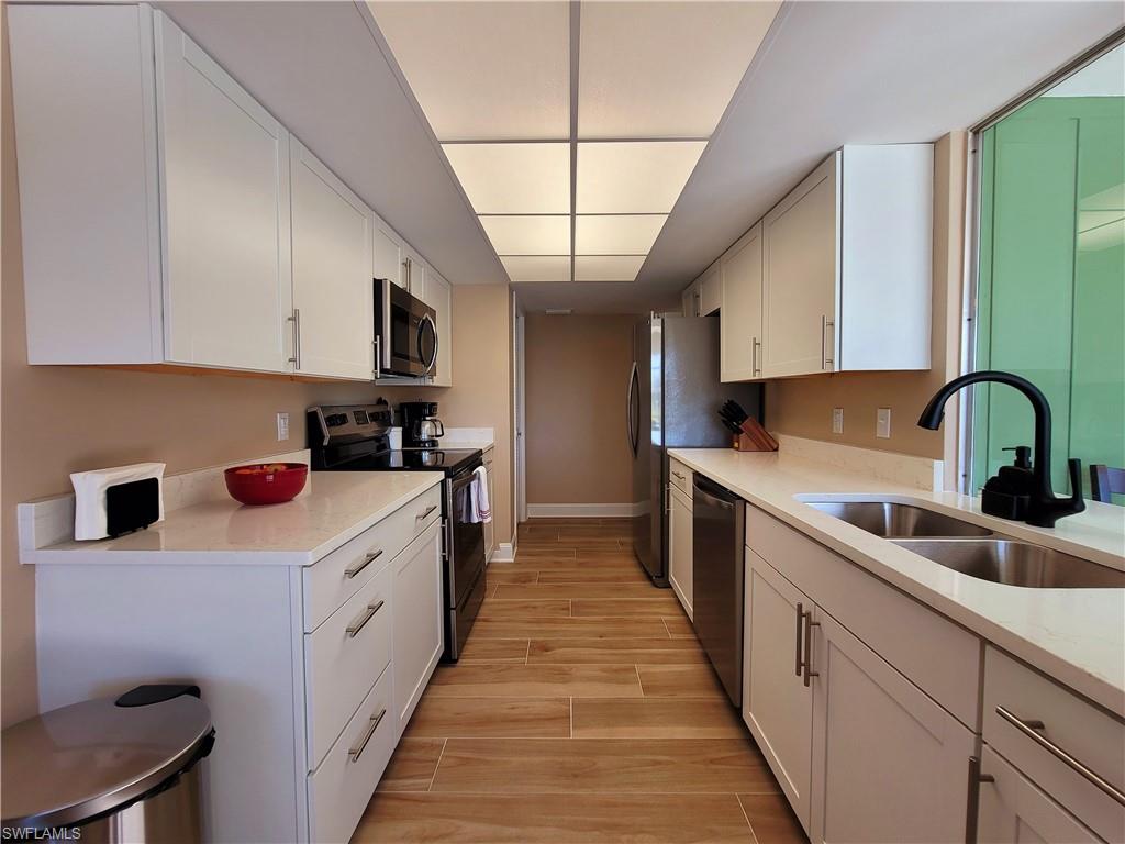 Galley kitchen featuring white cabinetry, light-toned countertops, wood-finish flooring, stainless steel appliances, and a double basin sink with a matte black faucet