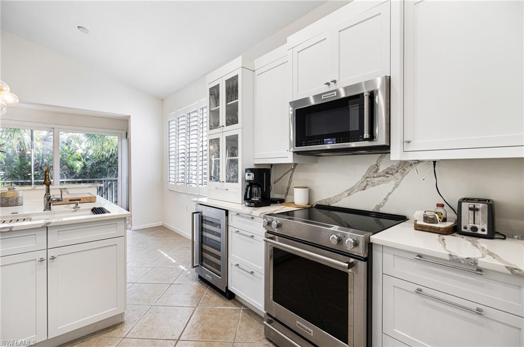 Kitchen with appliances with stainless steel finishes, white cabinetry, light tile patterned flooring, wine cooler, and lofted ceiling