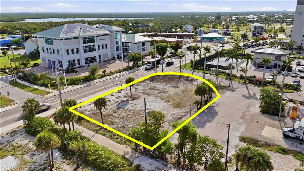 Vacant lot with street frontage, featuring mature palm trees and direct proximity to established commercial structures - Virtually Edited Image