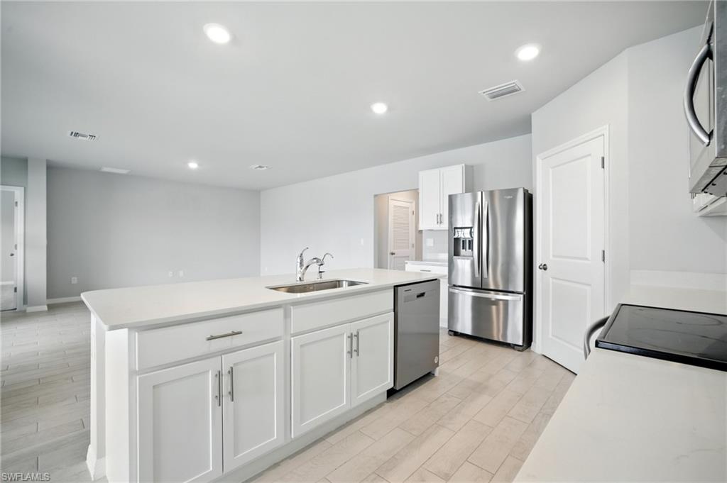 Kitchen island featuring a stainless steel sink with a high-arc faucet, white shaker cabinetry, and a light-toned countertop