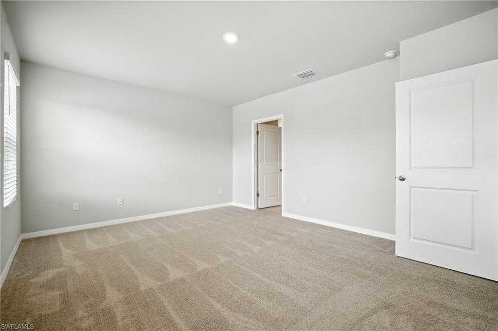 Spacious interior room with neutral-toned carpeting, white baseboards, and light gray wall paint
