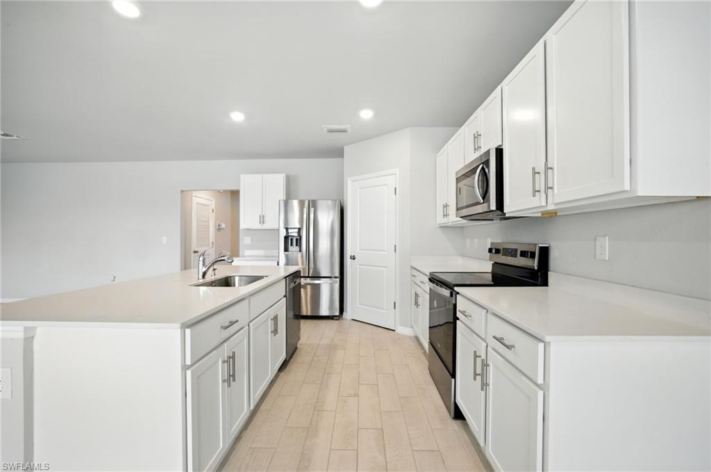 Modern kitchen featuring white cabinetry, light-toned countertops, stainless steel appliances, and wood-finish flooring