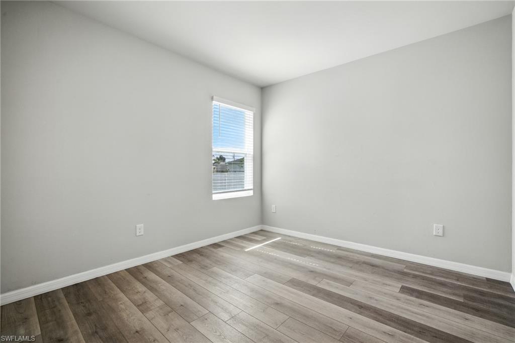 Room featuring wood-finish flooring, light gray walls, white baseboards, and a window with horizontal blinds
