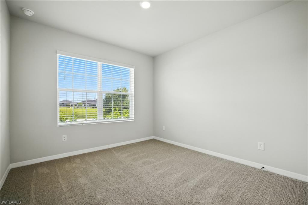 Light-filled interior space with neutral-toned walls, plush carpet flooring, and a large window featuring horizontal blinds