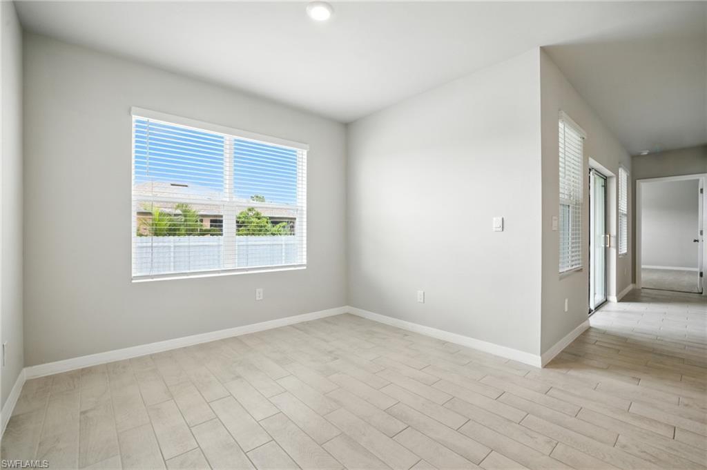 Spacious room with light gray walls, large window with horizontal blinds, recessed ceiling light, wood-finish tile flooring, and a glass sliding door