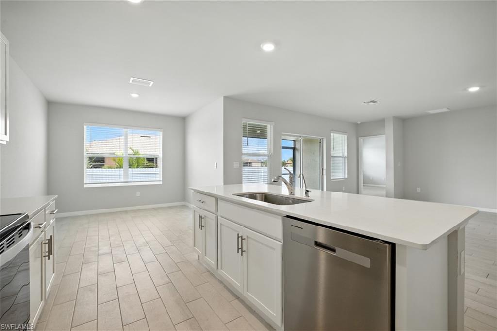 Kitchen island with integrated stainless steel sink and appliance, white cabinetry, and light-toned countertops