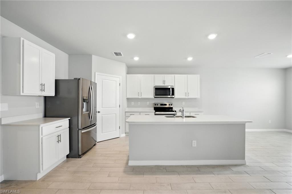 Modern kitchen featuring white cabinetry, stainless steel appliances, a center island with sink, ample counter space, and wood-finish flooring