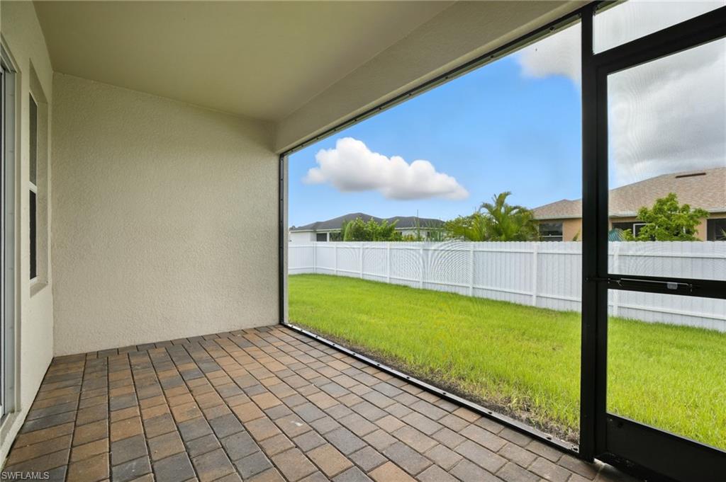 Screened lanai featuring multi-tone paver flooring, textured exterior wall, and a full-height vinyl privacy fence enclosing a manicured lawn