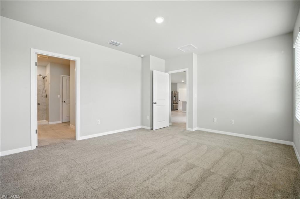 Spacious room featuring neutral carpet flooring, light gray walls, white baseboards, and overhead recessed lighting