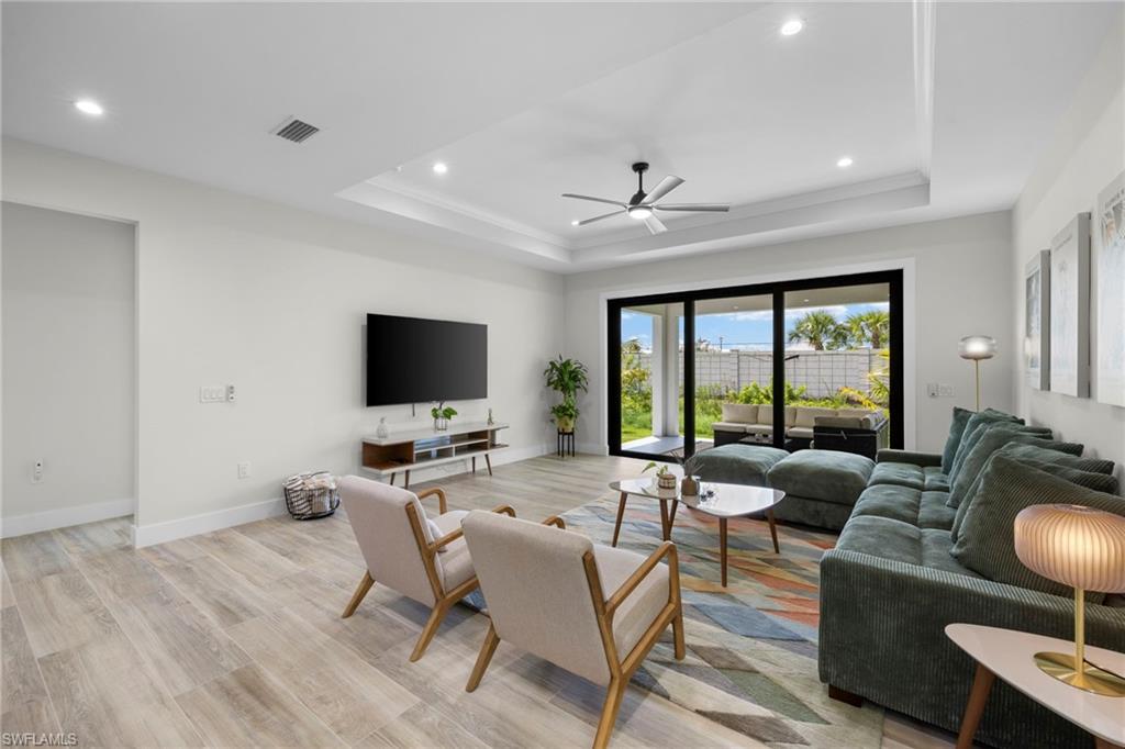 Living space featuring wood-finish flooring, recessed lighting, and a tray ceiling with a ceiling fan