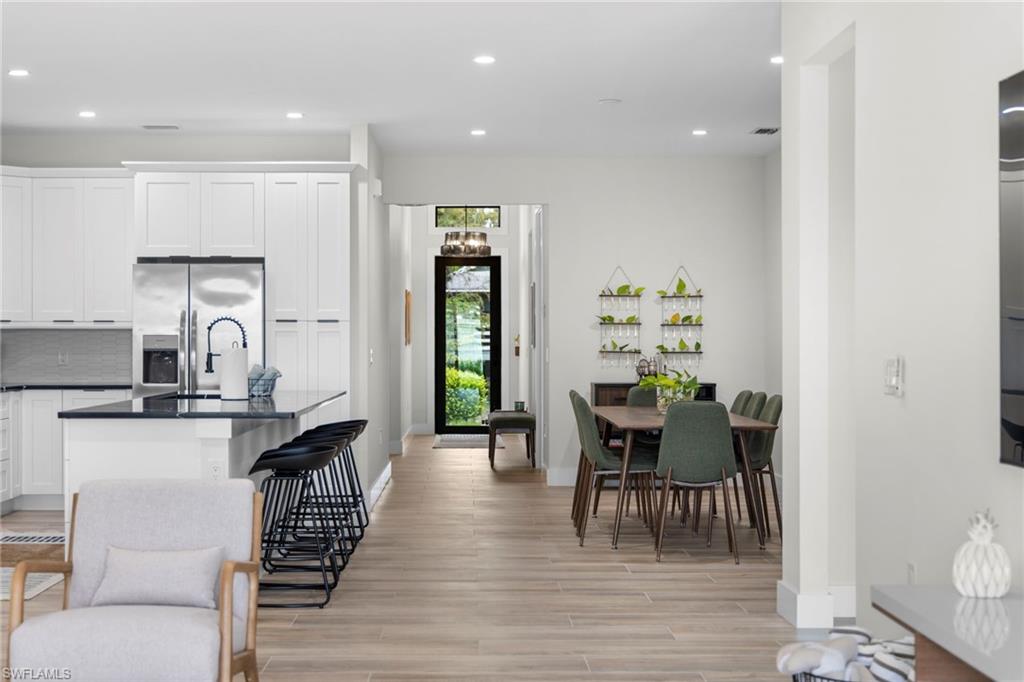 Open-concept interior featuring wood-finish flooring, white cabinetry, a kitchen island with seating, recessed lighting, and a prominent entry door with transom window