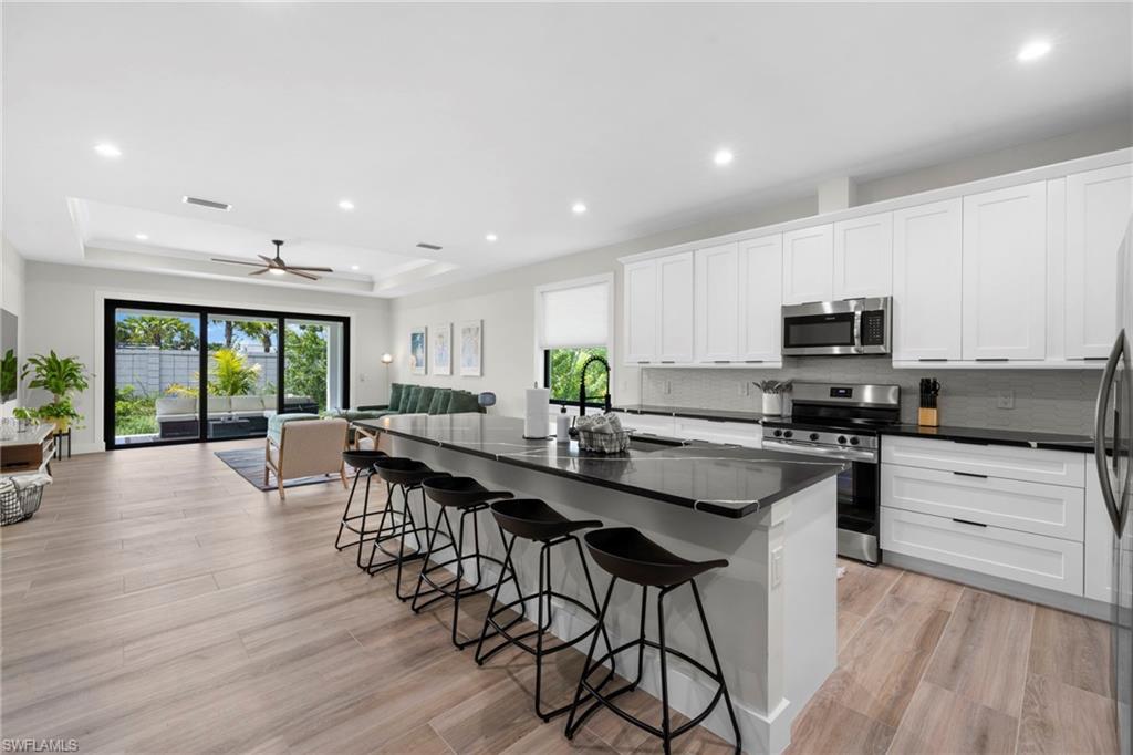 Contemporary kitchen featuring white cabinetry, stainless steel appliances, dark countertops, and a large island with seating