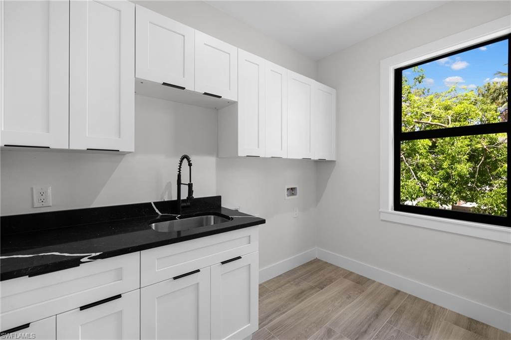 Modern utility room featuring white shaker cabinetry, dark stone countertops with a single basin sink, matte black faucet, and wood-finish tile flooring