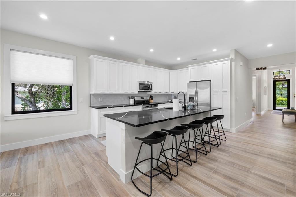 Kitchen featuring white cabinetry, dark countertops, a large island with seating, stainless steel appliances, and wood-finish flooring