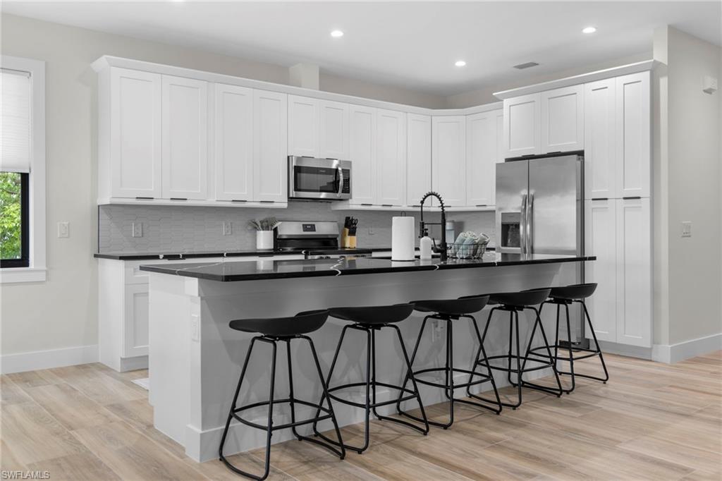 Modern kitchen featuring white shaker-style cabinetry, dark countertops, a large island with seating, stainless steel appliances, and wood-finish flooring