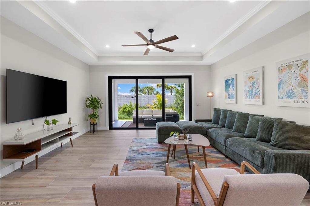 Spacious room featuring tray ceilings with recessed lighting, wood-finish flooring, and expansive sliding glass doors