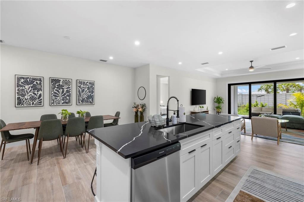 Open-concept living space featuring a central kitchen island with a dark countertop and integrated sink, stainless steel dishwasher, wood-finish flooring, and expansive sliding glass doors
