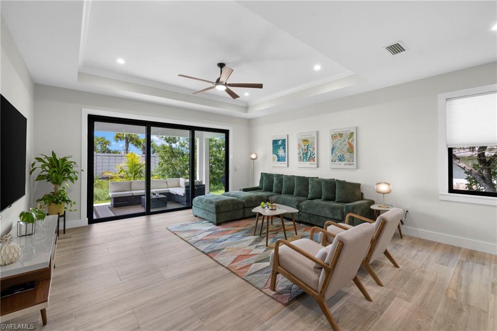 Open-concept living area featuring wood-finish flooring, a tray ceiling with recessed lighting, and a modern ceiling fan