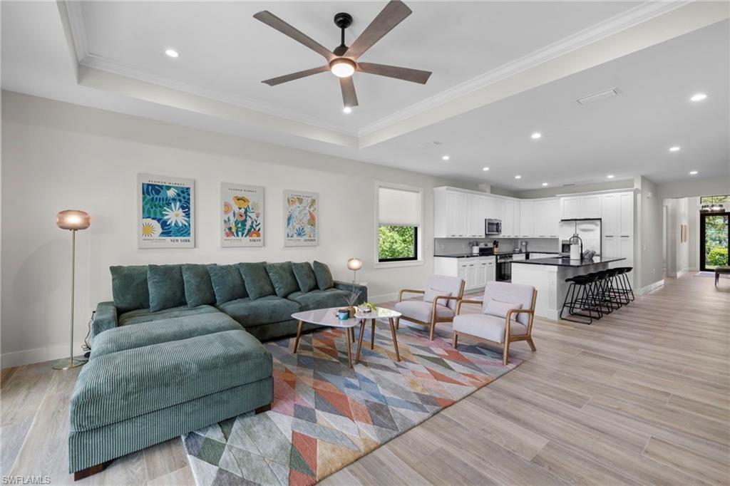 Open-concept interior featuring wood-finish flooring, a tray ceiling with a ceiling fan, recessed lighting, white cabinetry, and a dark kitchen island with seating