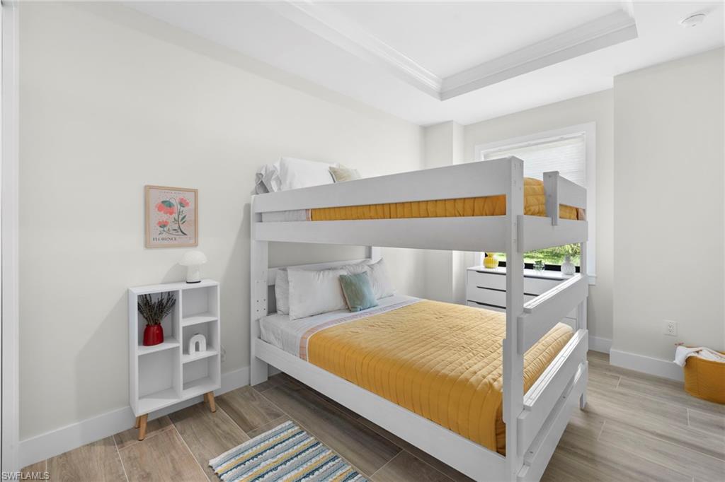Room featuring a white bunk bed, light wood-finish tile flooring, a window with a white frame, and a tray ceiling with crown molding