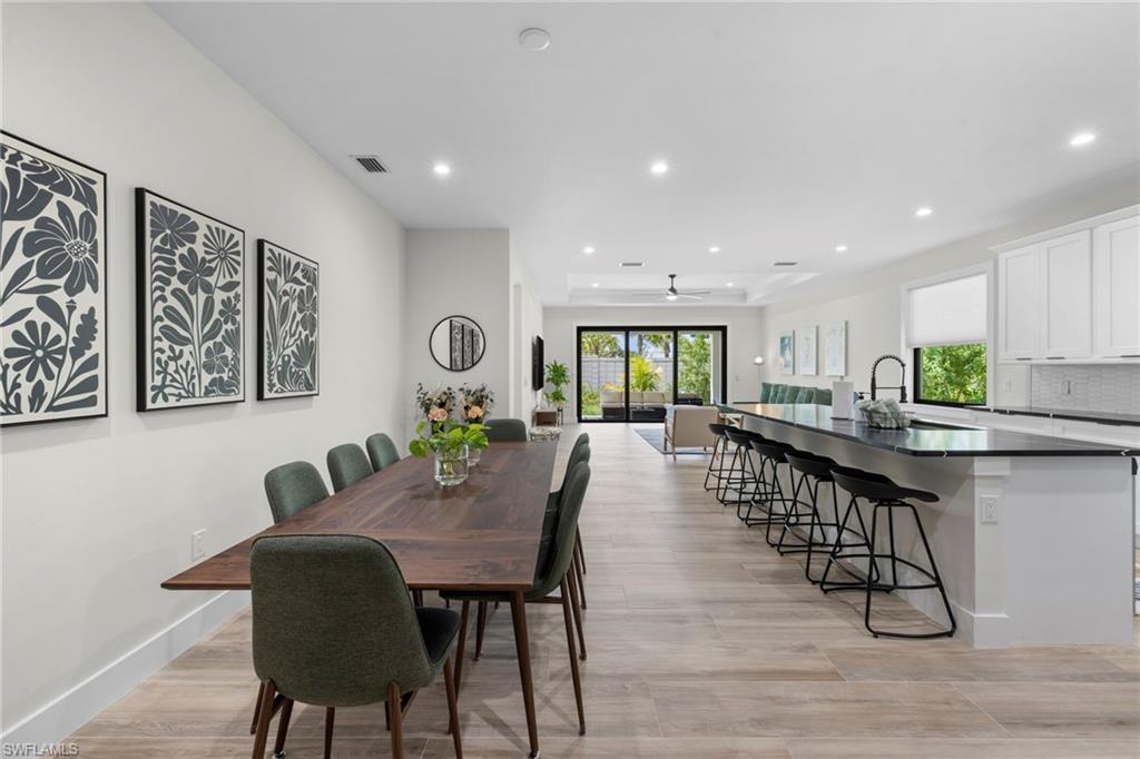 Open-concept living area featuring light wood-finish flooring, recessed lighting, and a contemporary kitchen with white cabinetry and dark countertops