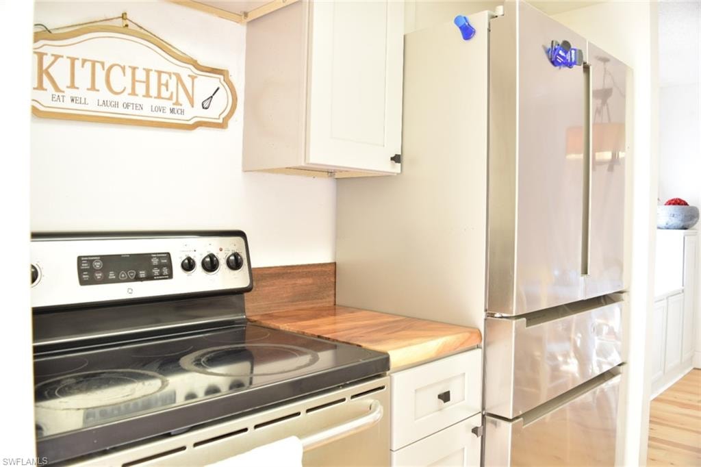 Kitchen featuring a stainless steel electric range, wood-finish countertops, light-colored cabinetry with dark hardware, and a stainless steel French door refrigerator
