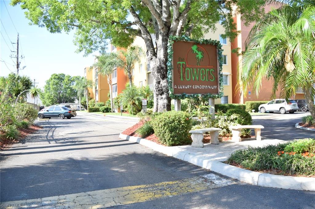 The Towers condominium entrance featuring a prominent sign framed by lush foliage and mature trees