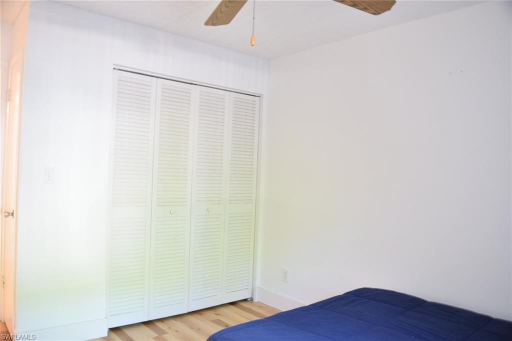 Bedroom featuring louvered bi-fold closet doors, light wood-finish flooring, and a ceiling fan with wood-finish blades