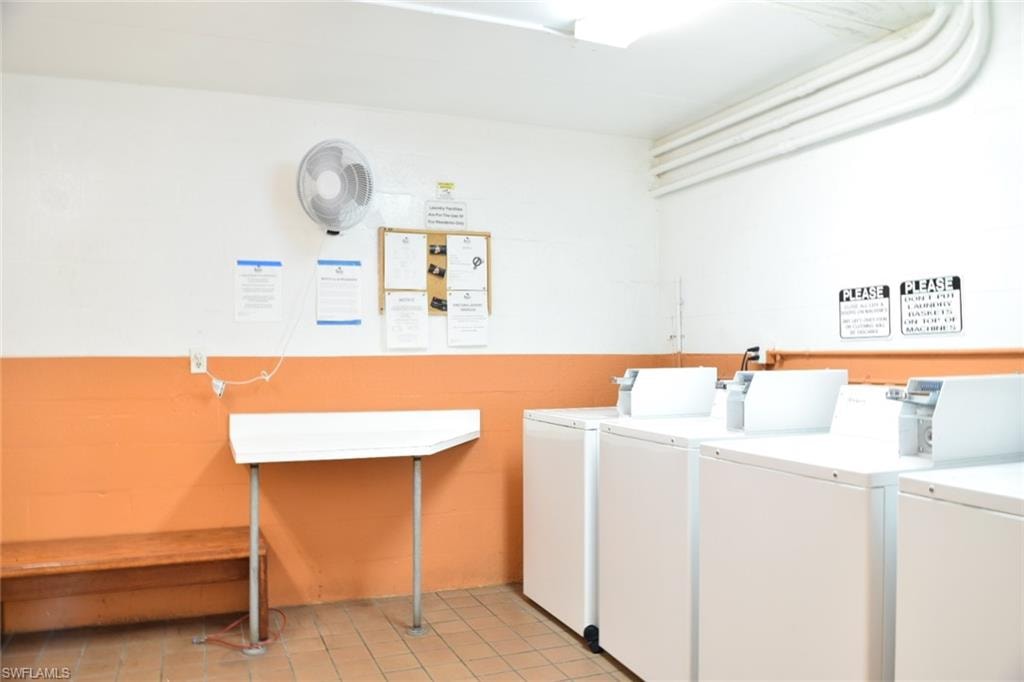 Community laundry room featuring multiple white washing machines, tiled flooring, and a white and orange two-tone wall finish