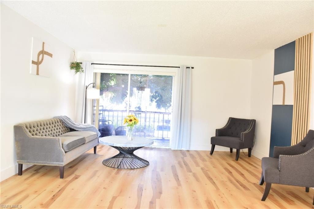 Bright living space featuring light wood-finish flooring, white walls, and a sliding glass door leading to a balcony
