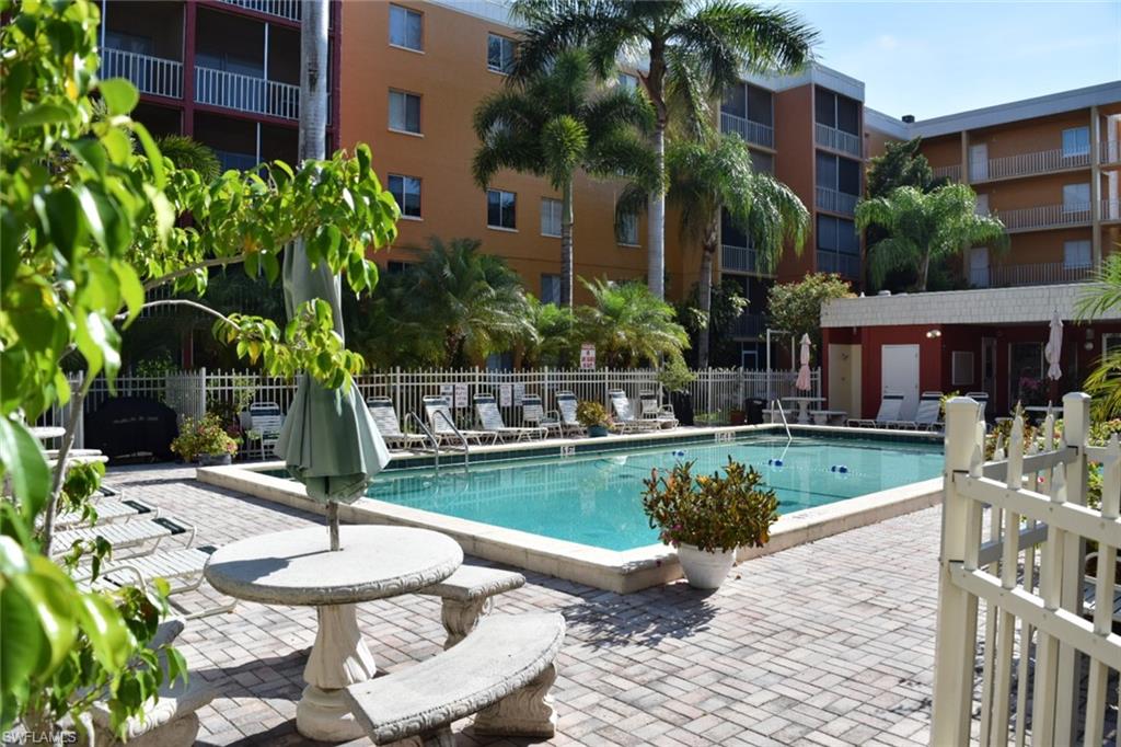 Swimming pool with a paved patio surround, featuring multiple lounge chairs and a white picket fence