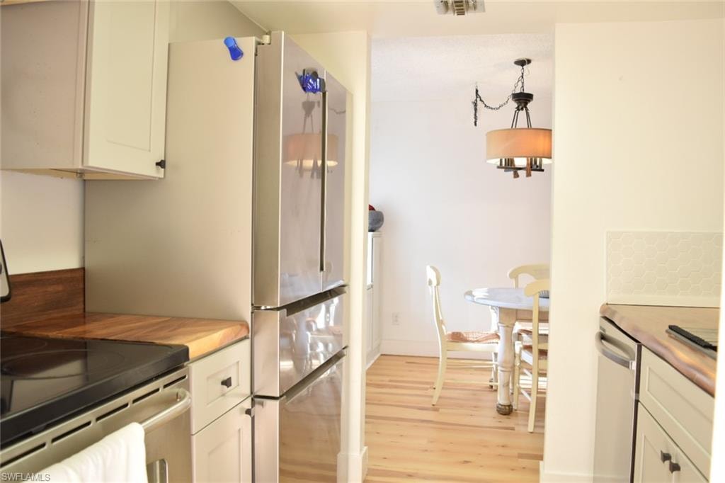 Stainless steel refrigerator in a kitchen featuring light wood-finish countertops and white cabinetry