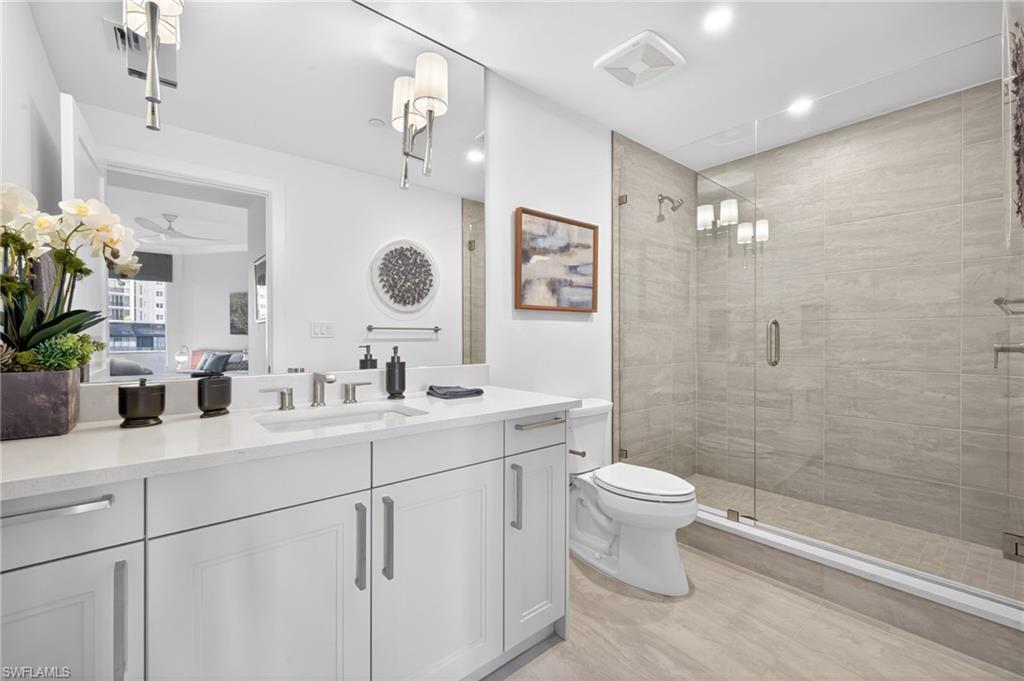 Contemporary bathroom featuring a spacious glass-enclosed shower with tiled walls and a large vanity with a white countertop and double-door cabinetry