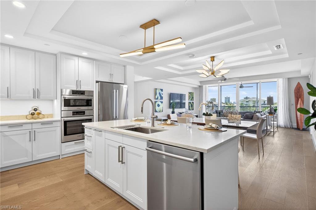 Contemporary kitchen featuring white cabinetry, stainless steel appliances, and a central island with modern light fixture and tray ceiling