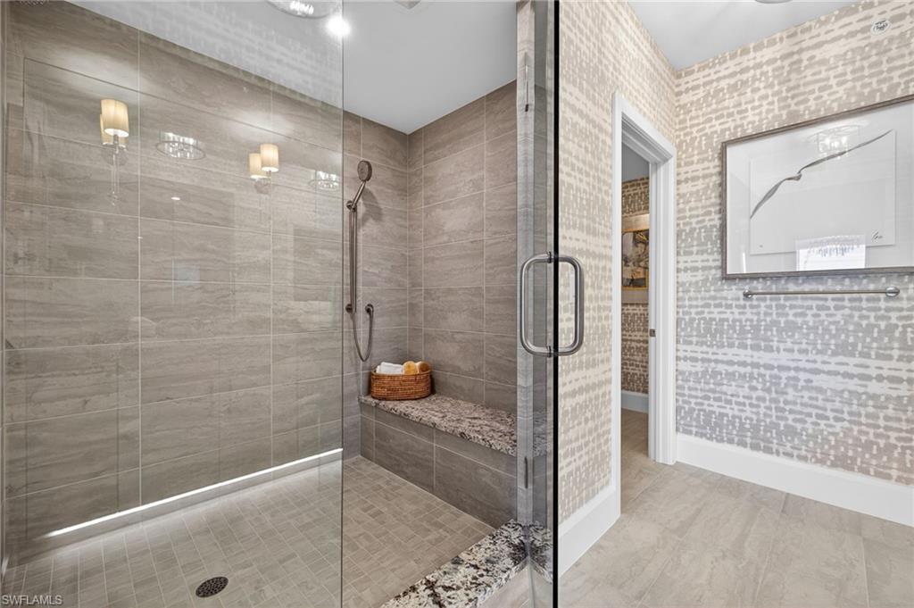 Master suite bathroom has a spacious walk-in shower with full-height tile surround, integrated bench with stone top, and clear glass enclosure with polished chrome hardware
