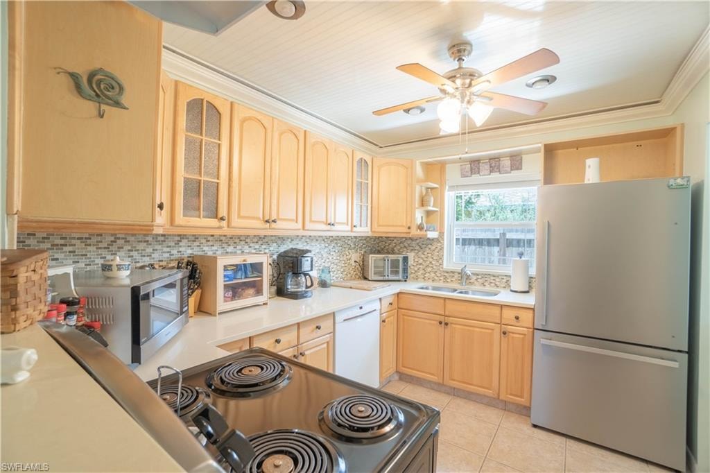 Kitchen featuring glass insert cabinets, freestanding refrigerator, light brown cabinets, light countertops, and ornamental molding
