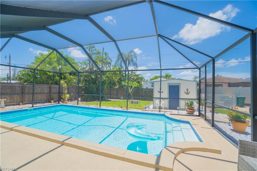 View of swimming pool with a storage shed, a fenced backyard, glass enclosure, and a sunroom