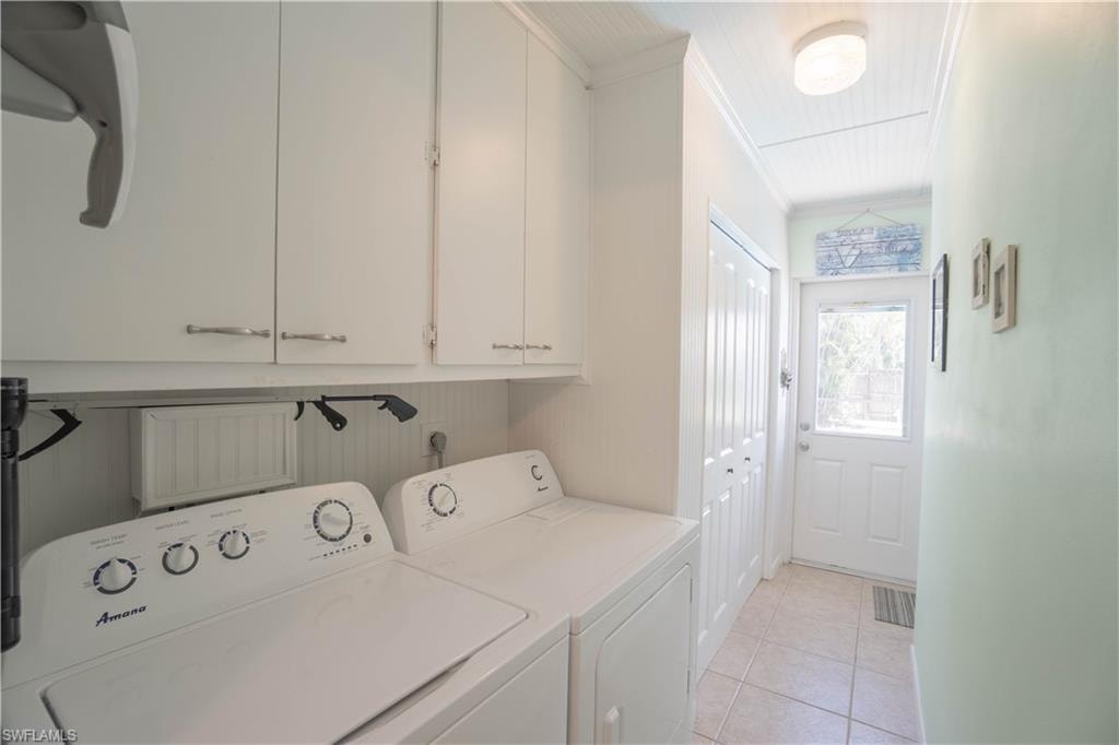 Laundry room featuring ornamental molding, light tile patterned floors, washing machine and clothes dryer, and cabinet space