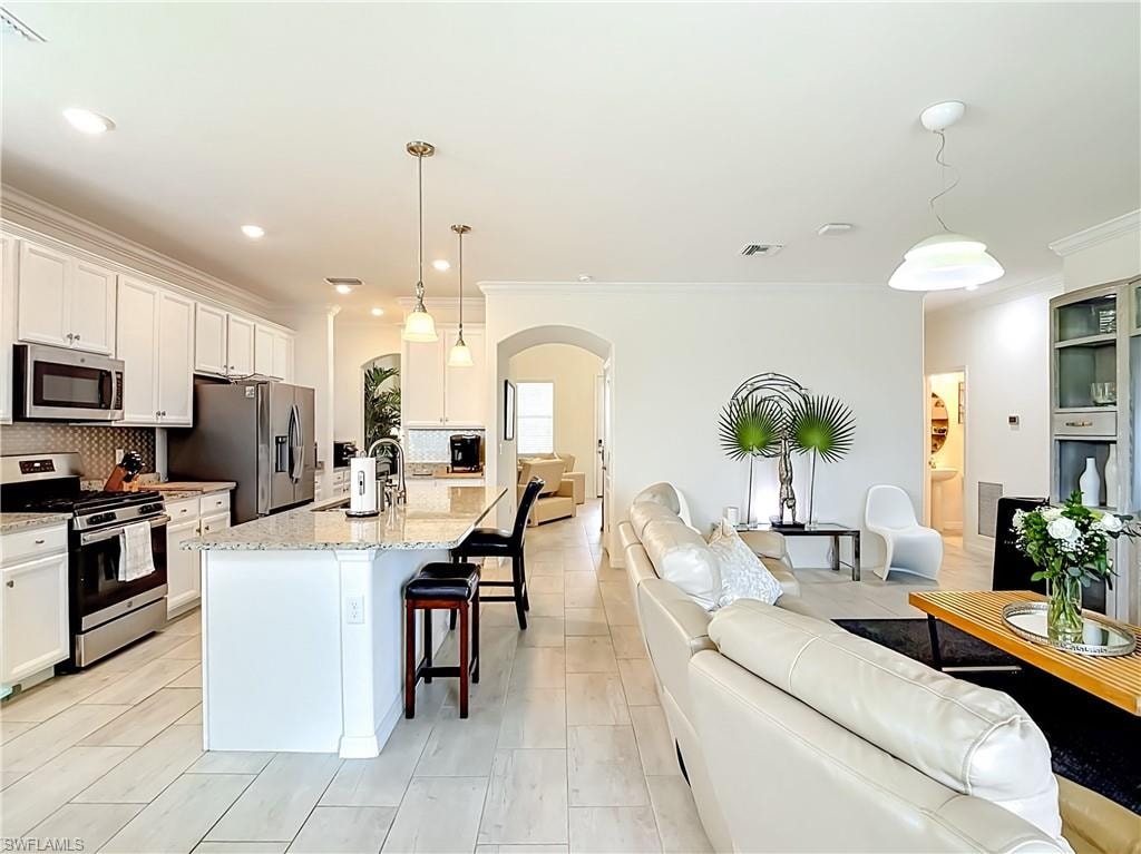 Spacious kitchen featuring white cabinetry, stainless steel appliances, a tiled backsplash, and a large island with a light-colored countertop