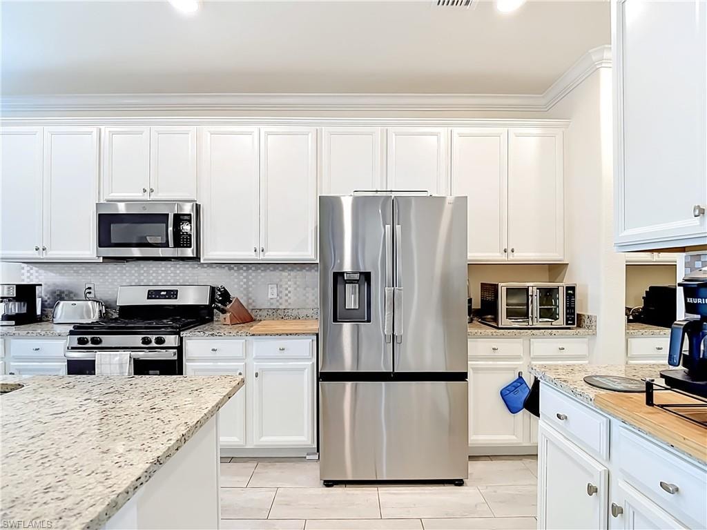 Kitchen featuring white shaker-style cabinetry, granite countertops, stainless steel appliances, a mosaic tile backsplash, and light-toned tile flooring