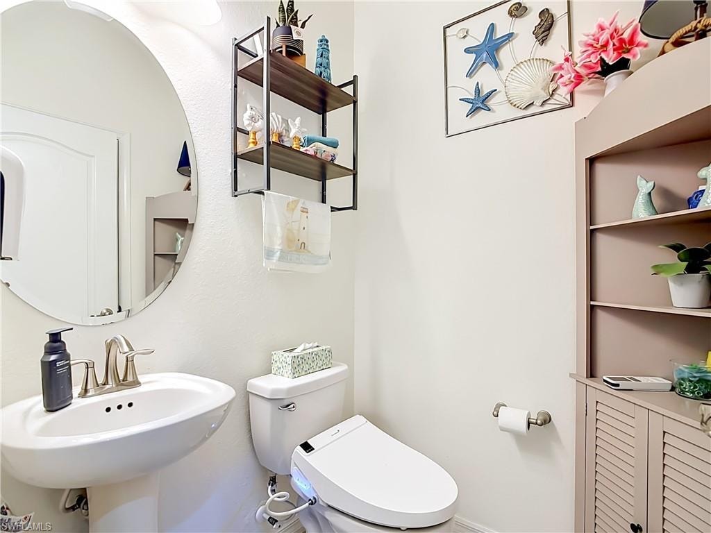 1st half bath room. Pedestal sink with brushed nickel faucet, oval mirror, wall-mounted light fixture, and tile flooring