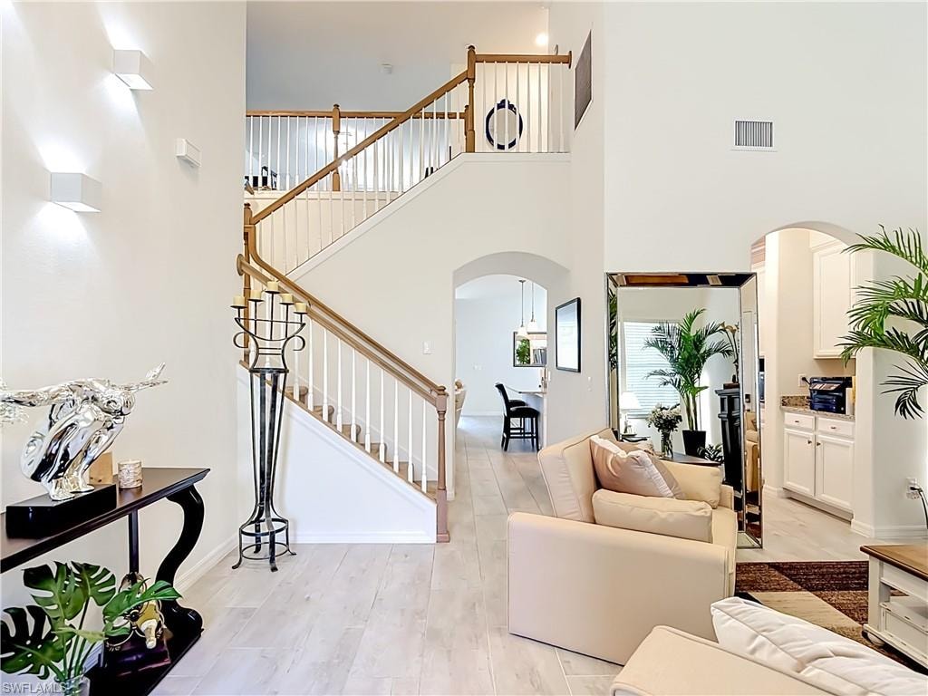 Two-story foyer featuring a staircase with wood-finish handrails and white balusters, light wood-finish flooring, and arched doorways
