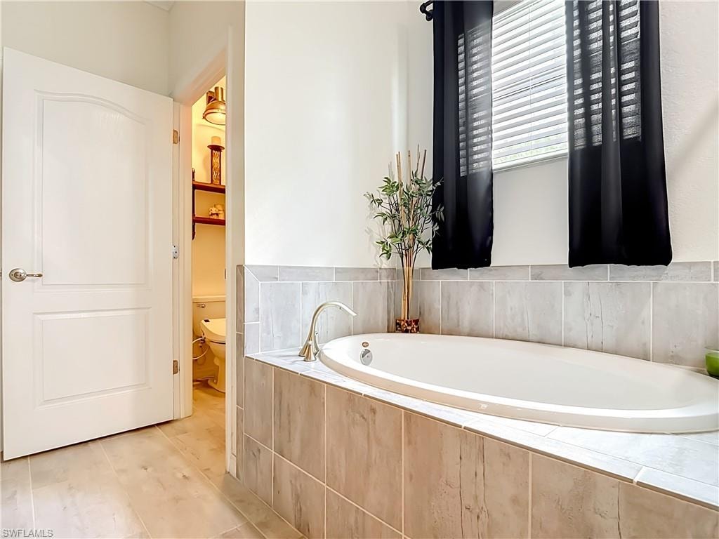Built-in soaking tub featuring light-toned tile surround, a brushed nickel faucet, and a window with blinds