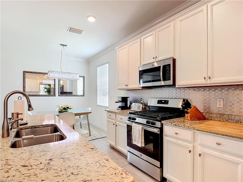 Kitchen featuring granite countertops, stainless steel appliances, white cabinetry, and a tile backsplash