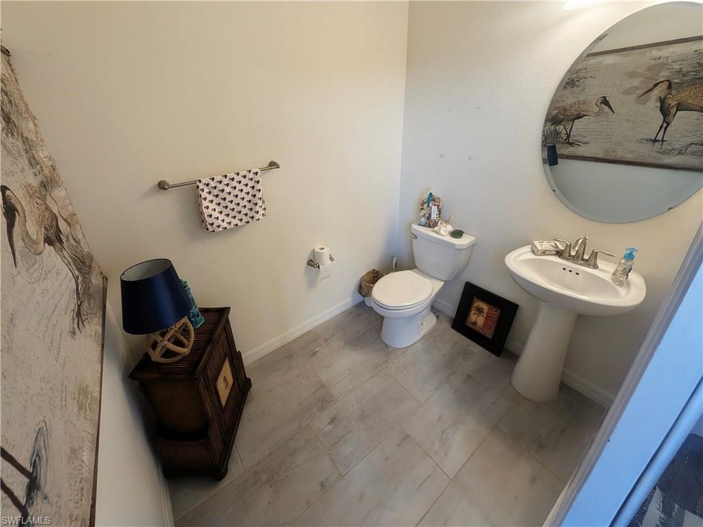 2nd half bathroom located on lanai. Bathroom featuring light gray wood-finish flooring, a white pedestal sink with dual-handle faucet, and a white toilet