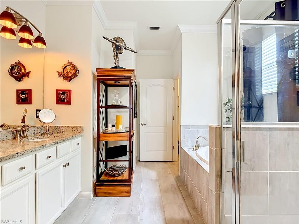 Bathroom featuring a double vanity with granite countertop, white cabinetry, a built-in soaking tub with tile surround, a glass-enclosed shower, and wood-finish flooring
