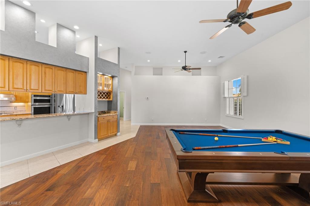 Open-concept living space featuring wood-finish flooring, a kitchen pass-through with a granite-look counter, built-in double ovens, a wine rack, and high ceilings with recessed lighting and ceiling fans