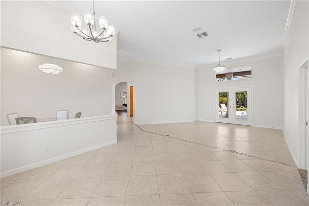Spacious living area featuring neutral tile flooring, high ceilings, crown molding, and double French doors leading to an outdoor area