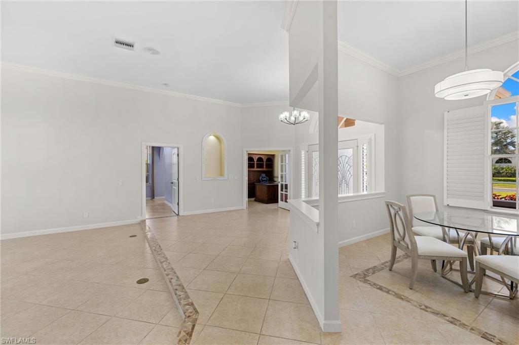 Bright interior with tiled flooring featuring an accent border, high ceilings with crown molding, and an arched wall niche