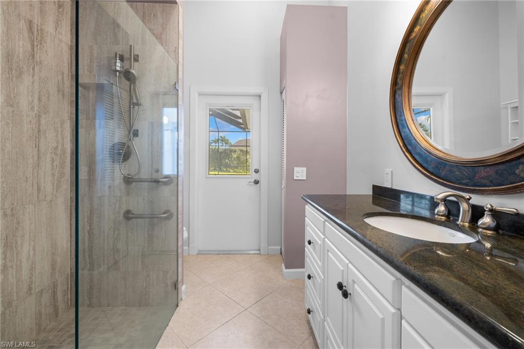 Bathroom #2 with access to outdoor living space featuring a frameless glass shower enclosure, wood-finish shower wall tile, brushed nickel fixtures, a single vanity with dark stone countertop, and a large decorative mirror